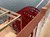 The image shows a red paddle wheel of a boat next to a railing, with the background of calm water.