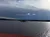 A calm lake stretches out under a cloudy sky, with a small tree-covered island in the distance.