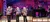 A musical group performs on stage wearing matching colorful sequin jackets.