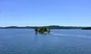 A small island with trees rises from a calm, expansive body of water under a clear blue sky.