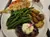 The image shows a plate with steak topped with butter, roasted potatoes, green beans, and skewered grilled shrimp, accompanied by a glass of iced tea.