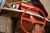 The image shows the interior of a wooden motorboat with red padded seats, a red steering wheel, and a wooden paddle.