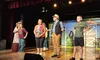 A group of people are performing a theatrical scene on stage, dressed in casual and Western-style clothing.