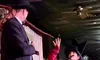 Two performers in Western-style costumes are engaged in a lively scene on stage, with one gesturing dramatically while the other looks on.