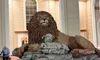 A large statue of a lion with a lamb lying beside it is prominently displayed, with a person using a walker passing by in the background.