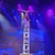 A performer balances in a handstand on top of a precarious stack of chairs under colorful stage lighting.