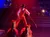 A person dressed in a cowboy outfit is performing a stunt by standing on two moving horses under dramatic red lighting.