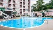This image shows a serene outdoor pool area with sun loungers and a fountain, flanked by a multi-story residential building with balconies.
