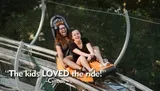 Two people are enjoying a thrilling ride on a mountain coaster, laughing joyfully as they descend the track.