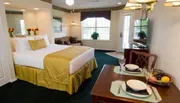This image shows a neatly arranged hotel or guest room with a double bed, dining setup for two, and a small living area in the background.
