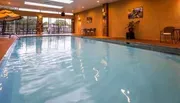 This is an image of an indoor swimming pool with calm water, surrounded by seating areas and framed by a warm, ambient interior.