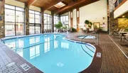 This image shows an indoor swimming pool area with lounge chairs, large windows, and a hot tub, reflecting a leisurely and comfortable atmosphere.