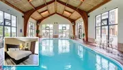 The image shows an indoor swimming pool with large windows and a wooden ceiling, overlaid with a smaller inset image of a bedroom with a bed, lamps, and curtains.