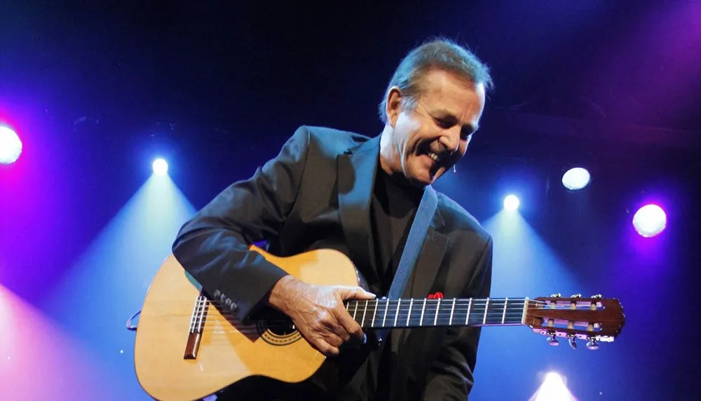 A person is joyfully playing a classical guitar on stage under colorful stage lights