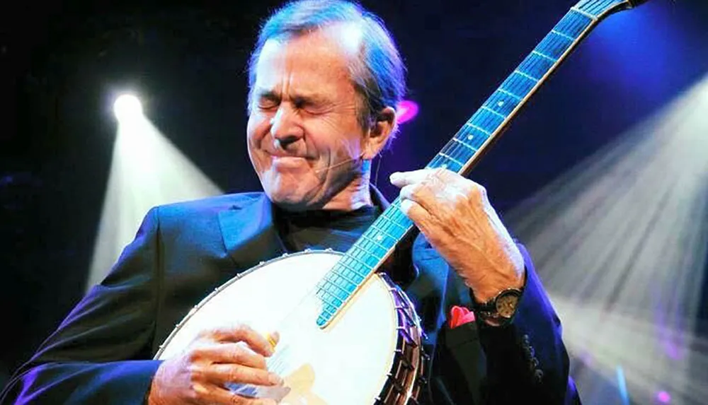 A musician is playing the banjo with a concentrated expression on stage under a spotlight