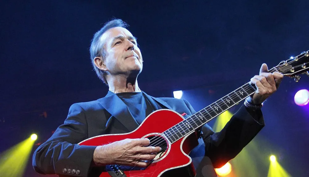 A musician is performing on stage with a red guitar under colorful stage lights