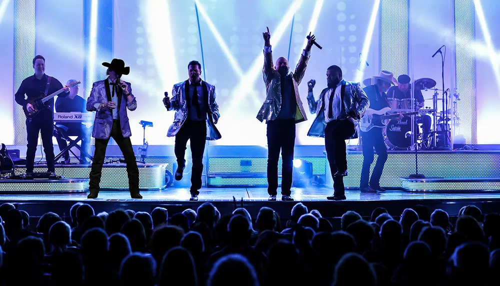 A band performs on stage engaging with an enthusiastic crowd under bright stage lights