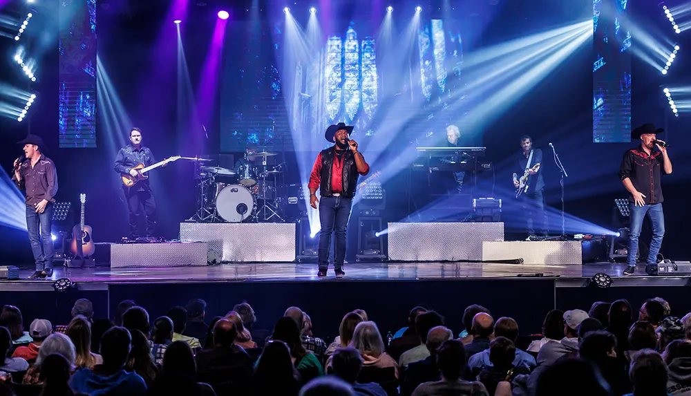 A country band performs on a colorful stage with multiple musicians and vocalists entertaining a seated audience