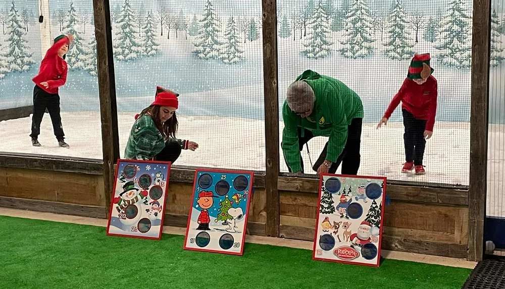Four people in festive attire are playing a bean bag toss game in a room decorated with a winter theme