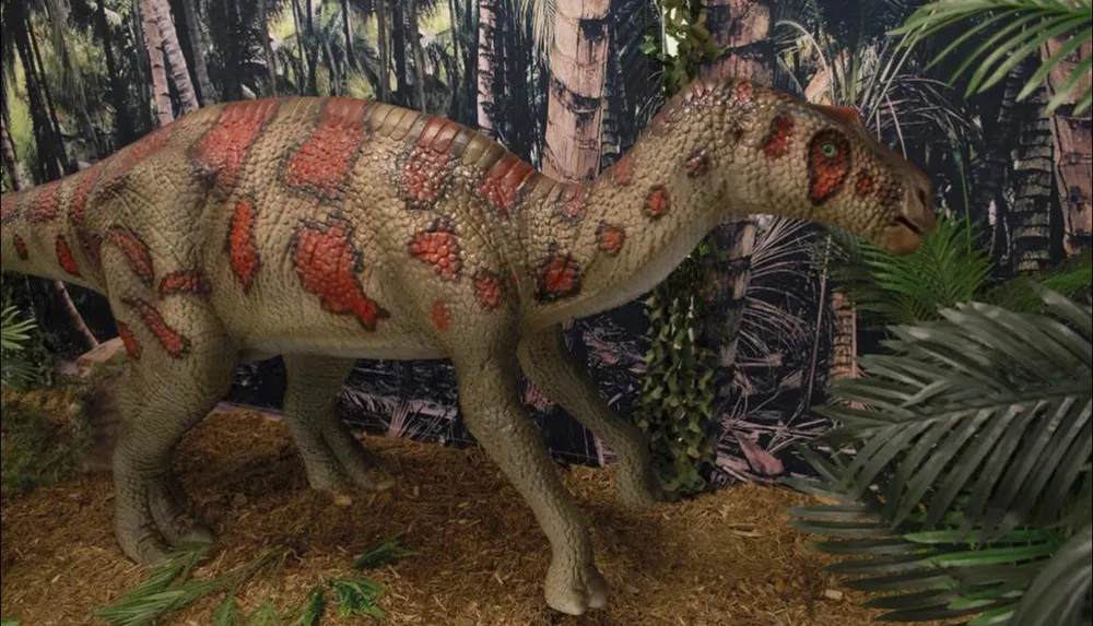 A life-sized model of a dinosaur with textured skin and reddish-brown patterns stands in a prehistoric jungle setting
