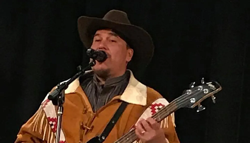 A person wearing a cowboy hat is performing music with a guitar and singing into a microphone
