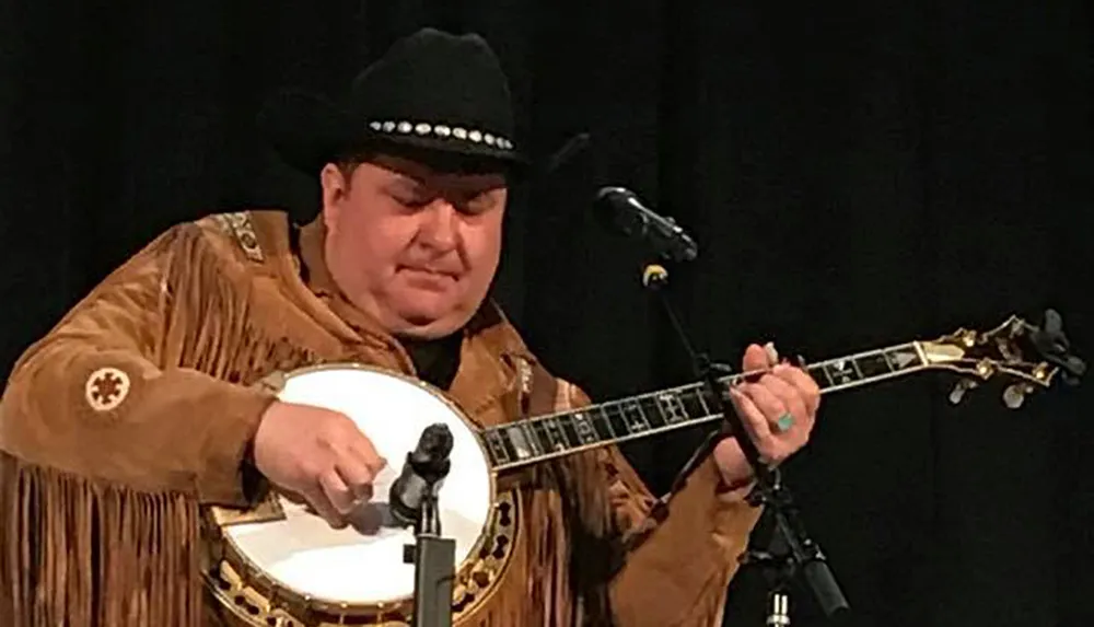 A musician wearing a cowboy hat and fringed leather jacket is playing a banjo onstage