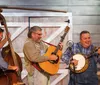 Three musicians playing a double bass guitar and banjo perform with visible enthusiasm in front of a wooden backdrop