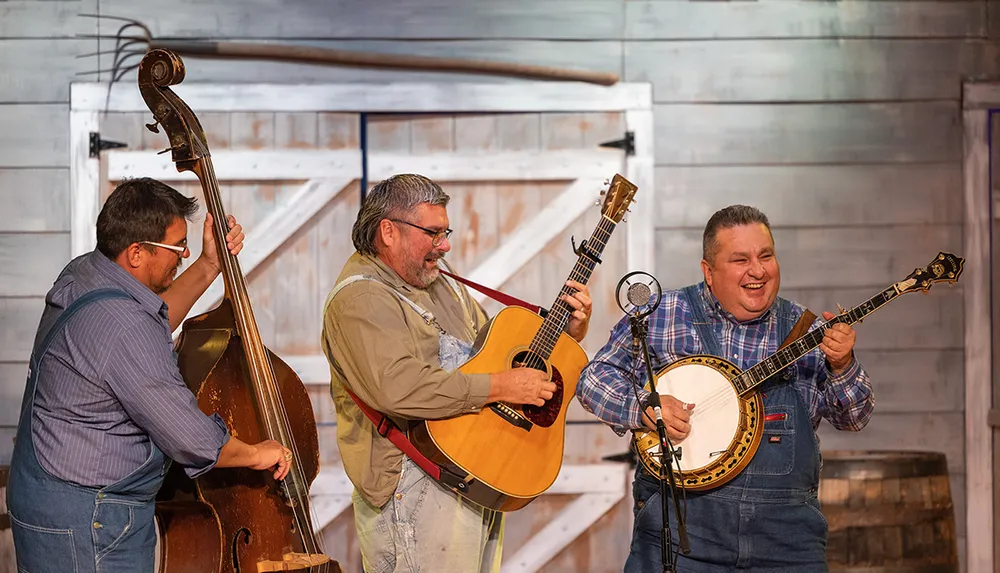 Three musicians playing a double bass guitar and banjo perform with visible enthusiasm in front of a wooden backdrop