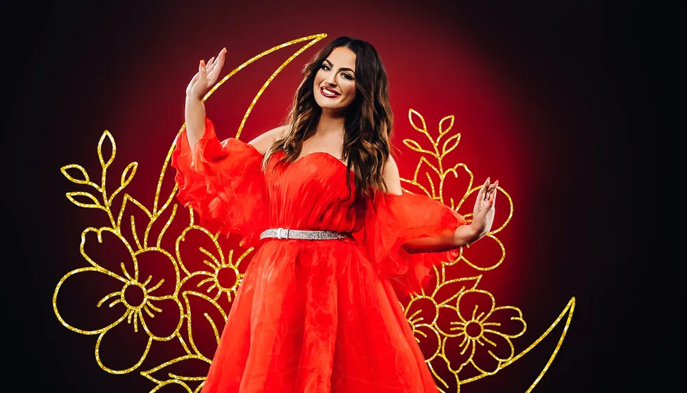 A smiling woman in a flowing red dress is striking a graceful pose against a dark background adorned with a floral golden outline