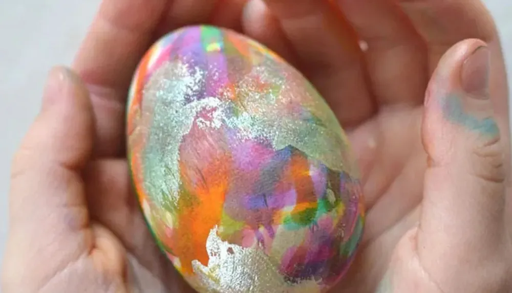A pair of hands holds a vibrantly colored shimmery painted egg