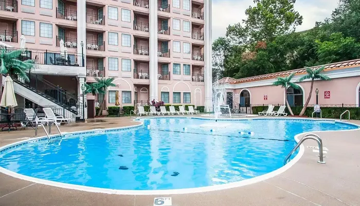 This image shows a serene outdoor pool area with sun loungers and a fountain flanked by a multi-story residential building with balconies