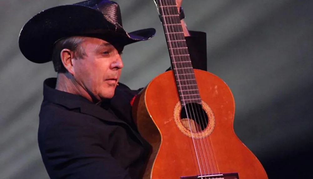 A person in a cowboy hat is holding a guitar onstage