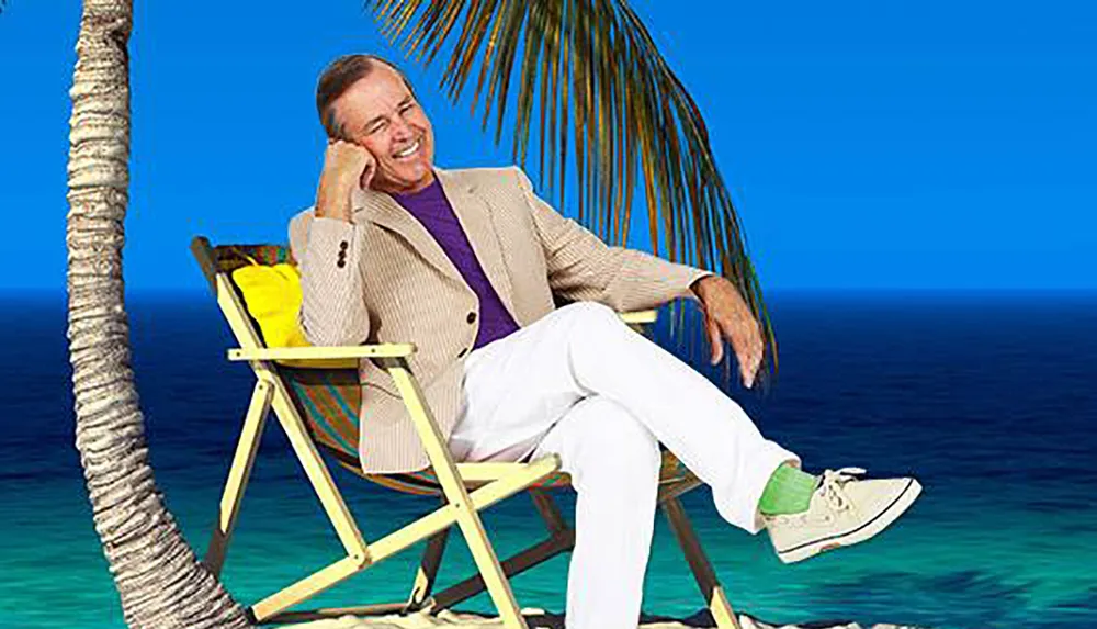 A person is smiling and relaxing on a beach chair next to a palm tree with a clear blue sky and sea in the background
