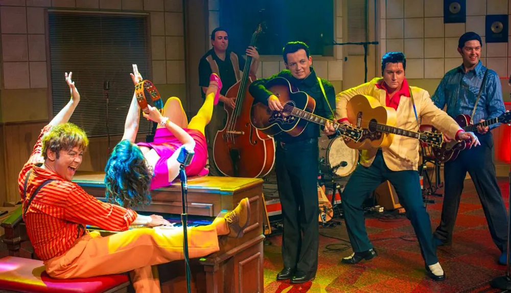 The image shows a vibrant and colorful scene with performers in retro-style attire enthusiastically playing music with one person lying on a piano playing keys upside down