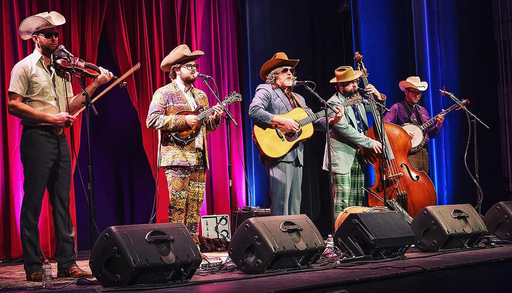 Four musicians in cowboy hats are performing on stage with a fiddle a mandolin an acoustic guitar and an upright bass
