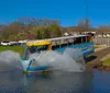 A duck boat filled with passengers is creating a splash as it enters the water from a ramp on a sunny day