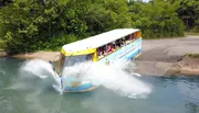 A duck boat filled with passengers is creating a splash as it enters the water from a ramp on a sunny day.