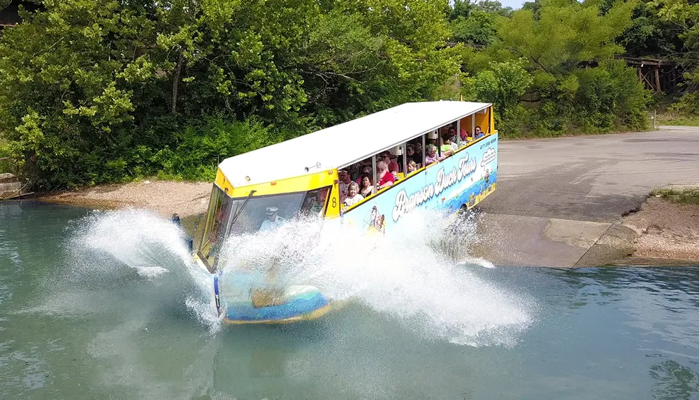 A duck boat filled with passengers is creating a splash as it enters the water from a ramp on a sunny day