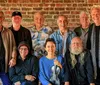 A group of smiling people including men and one woman holding a violin pose together against a brick wall backdrop