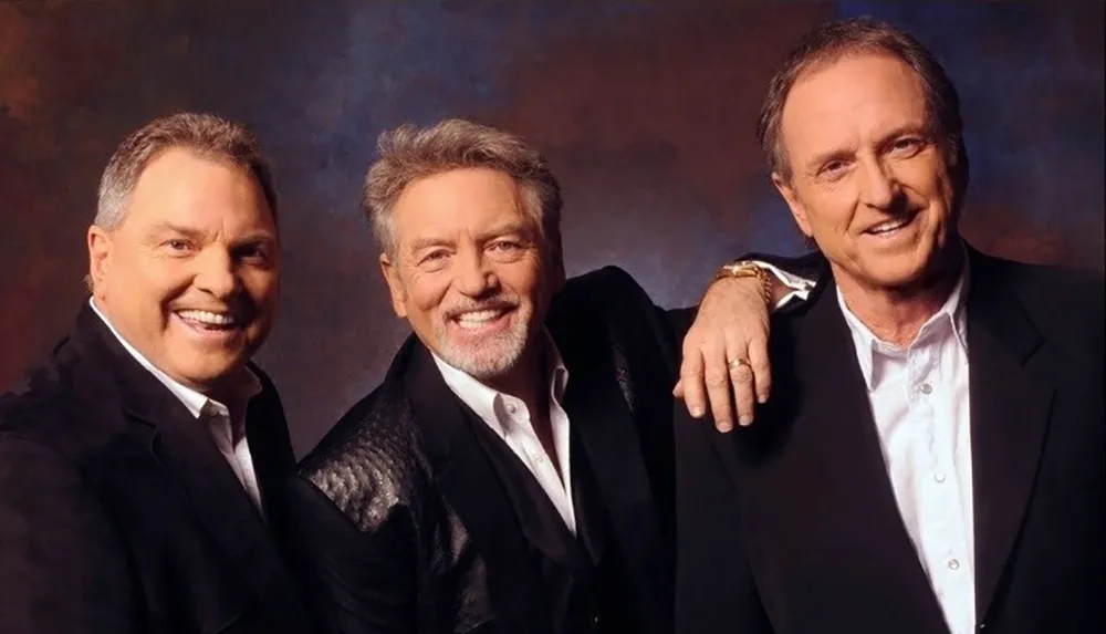 Three smiling men in suits pose companionably for a portrait style photo against a mottled backdrop