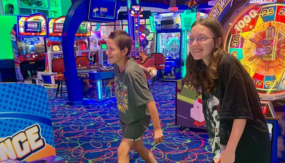 Two young people are smiling and playing in a vibrant arcade filled with colorful gaming machines