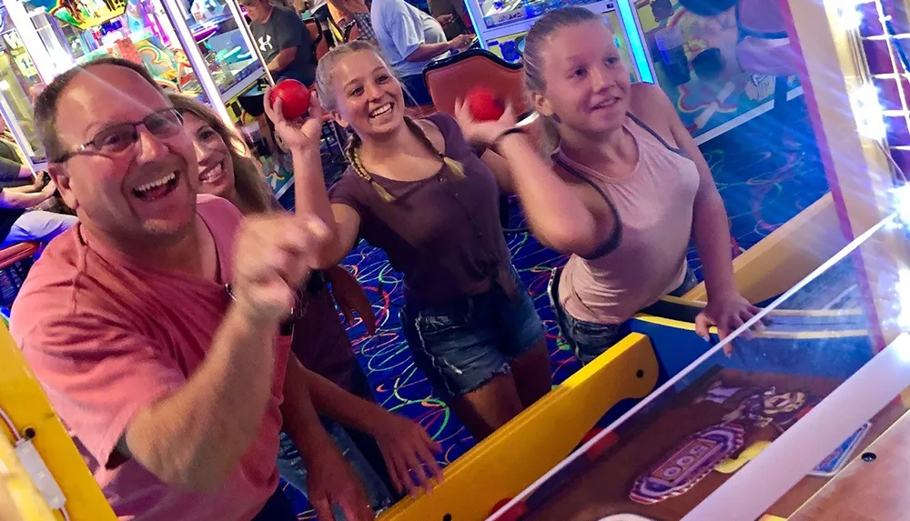 A group of four people are having fun playing skee-ball at an arcade with expressions of joy and excitement on their faces