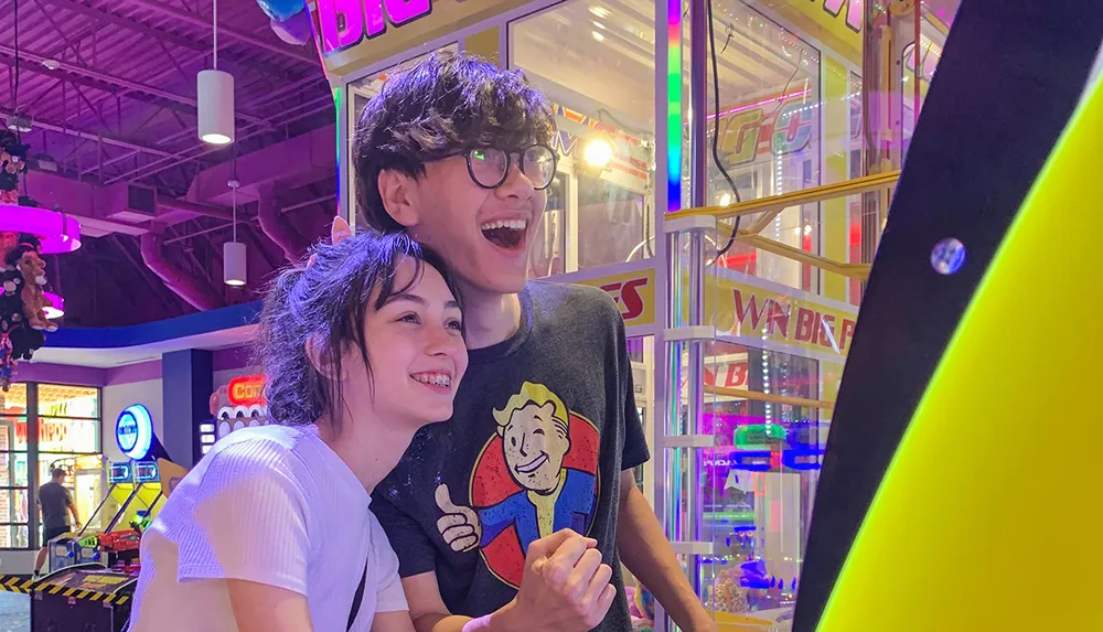 Two happy young people are enjoying a moment at an arcade surrounded by colorful lights and gaming machines
