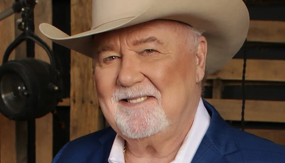 A smiling older man wearing a cowboy hat and a blue jacket poses for a portrait