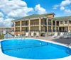 The image shows an outdoor swimming pool surrounded by lounge chairs with a two-story building in the background under a partly cloudy sky