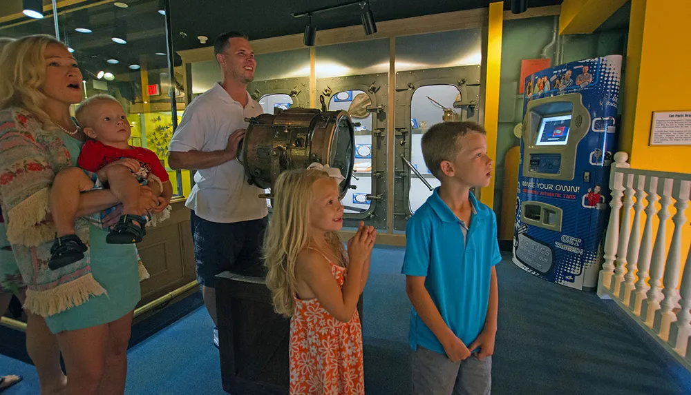 A family with two adults and three children appears engaged and interested in an exhibit they are viewing at a museum