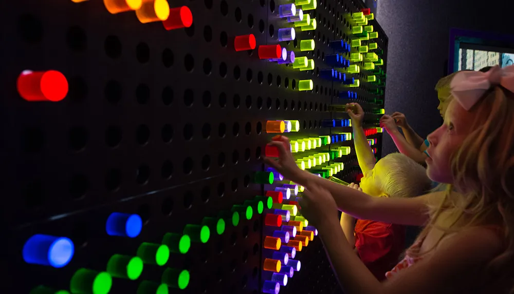 Children are interacting with a colorful illuminated pegboard activity in a dimly lit room