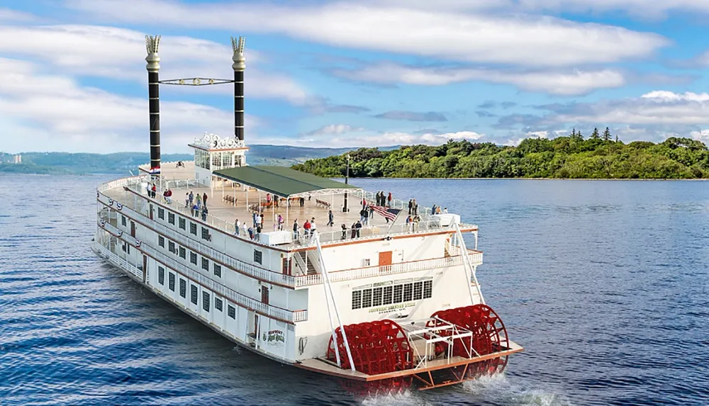 A paddle steamboat with passengers on deck sails across a river surrounded by lush greenery and under a blue sky