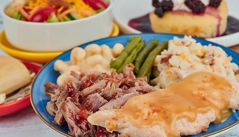A plate is filled with a variety of foods including mashed potatoes with gravy green beans macaroni and cheese shredded meat beside other dishes like a salad bread and dessert