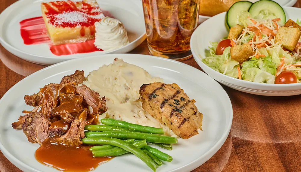 The image shows a meal consisting of grilled chicken beef with gravy mashed potatoes green beans a side salad a dessert with whipped cream and a drink
